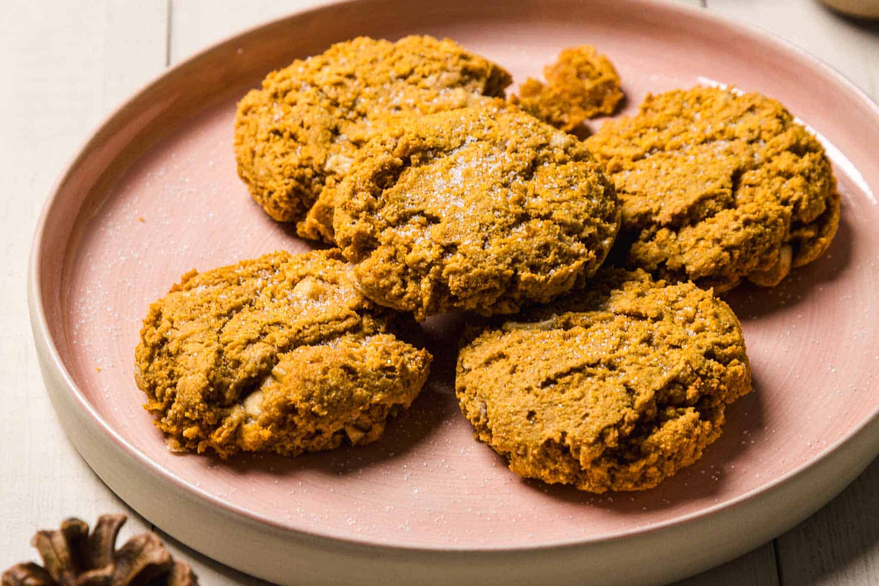 Five Pumpkin and White Chocolate Chip Cookies rest on a pink plate, arranged closely together atop a light wooden table.