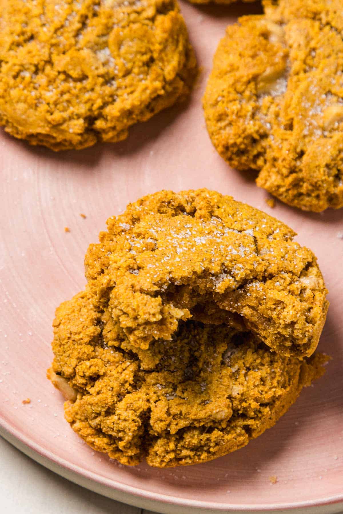 Close-up of golden brown Pumpkin and White Chocolate Chip Cookies on a pink plate, with one cookie showing a bite taken out.