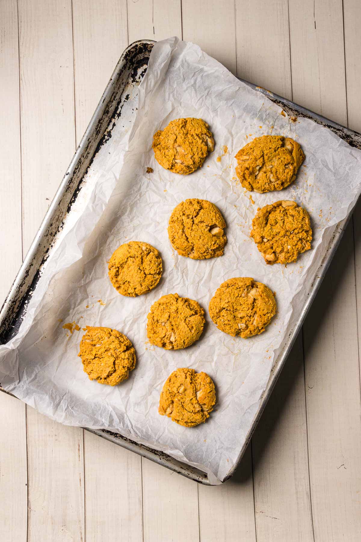 Nine golden brown Pumpkin and White Chocolate Chip Cookies rest on a parchment-lined baking sheet, set on a light wooden surface.