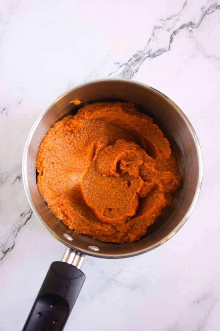 A saucepan filled with thick, orange-red tomato paste on a white marble surface, perfect for making savory bases or pairing with Pumpkin Br&ucirc;l&eacute;e Tarts.