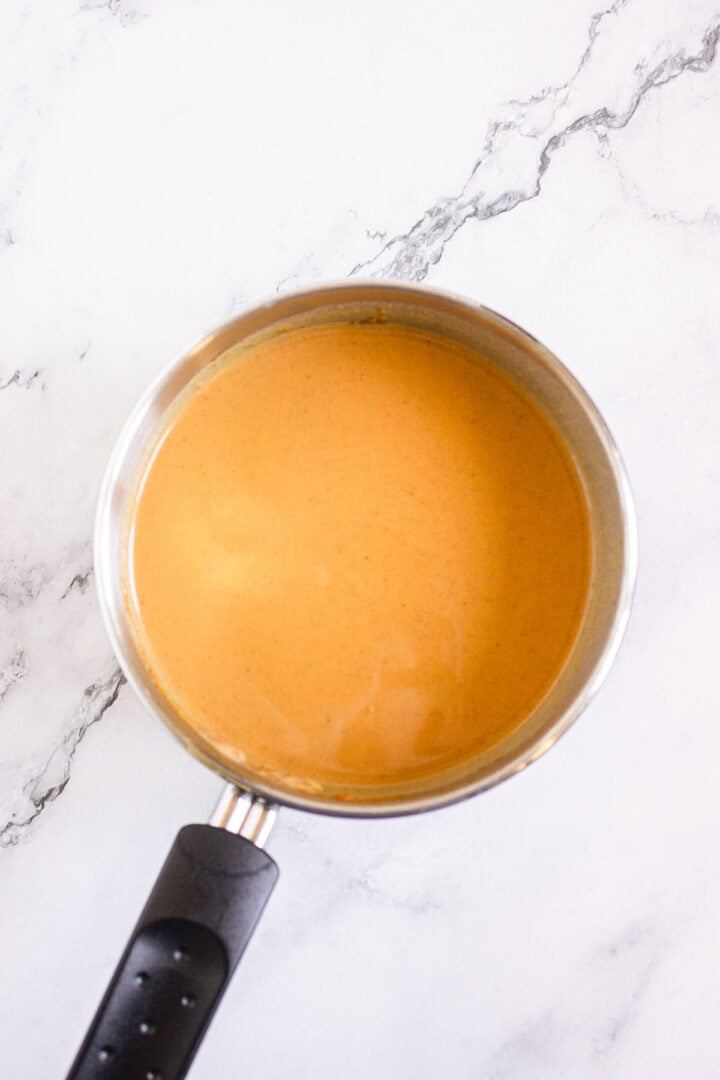 A saucepan filled with creamy orange sauce on a white marble surface, perfect for making Pumpkin Br&ucirc;l&eacute;e Tarts.
