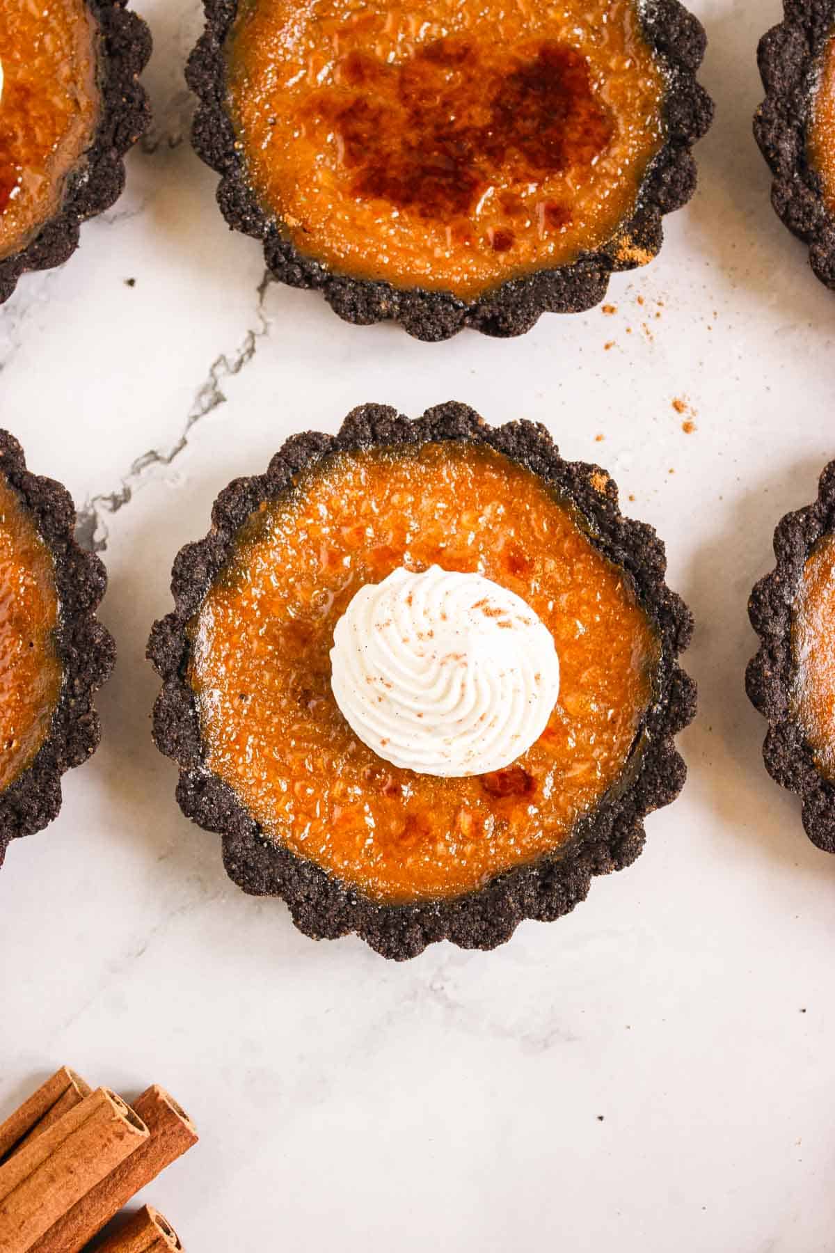 Pumpkin Br&ucirc;l&eacute;e Tarts with a caramelized top, chocolate crust, and a swirl of whipped cream in the center.