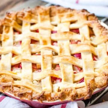 A freshly baked pie with a golden brown lattice crust sits on a wooden table with a white and red towel.