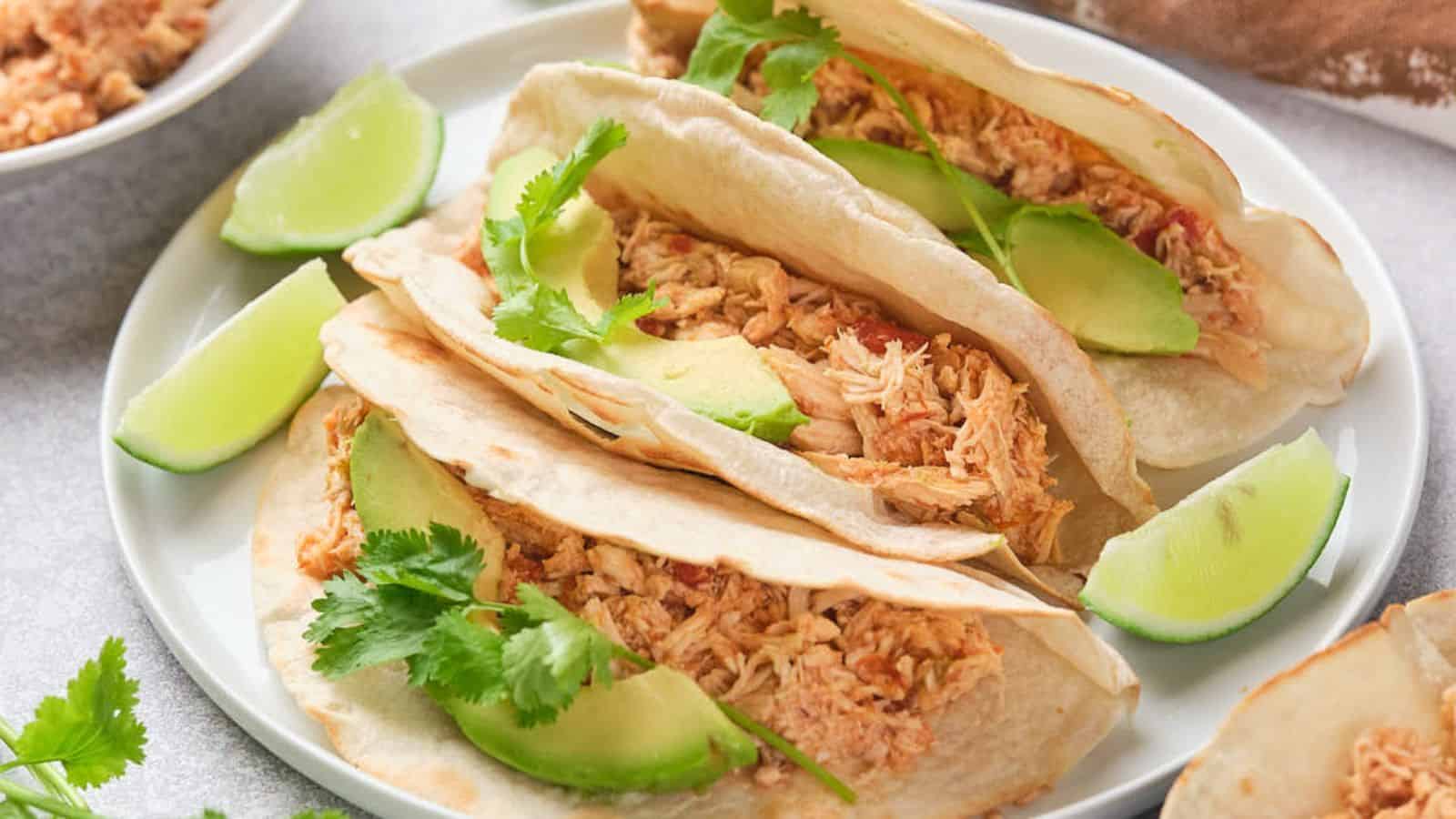 Close-up of shredded chicken with vegetables in a pan, being stirred with a wooden spoon.