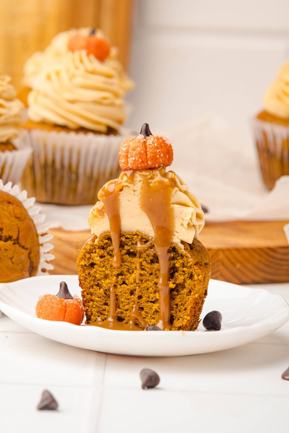 A pumpkin cupcake topped with caramel drizzle, frosting, and a small candy pumpkin&mdash;just like our Salted Caramel Pumpkin Muffins&mdash;cut in half on a plate.