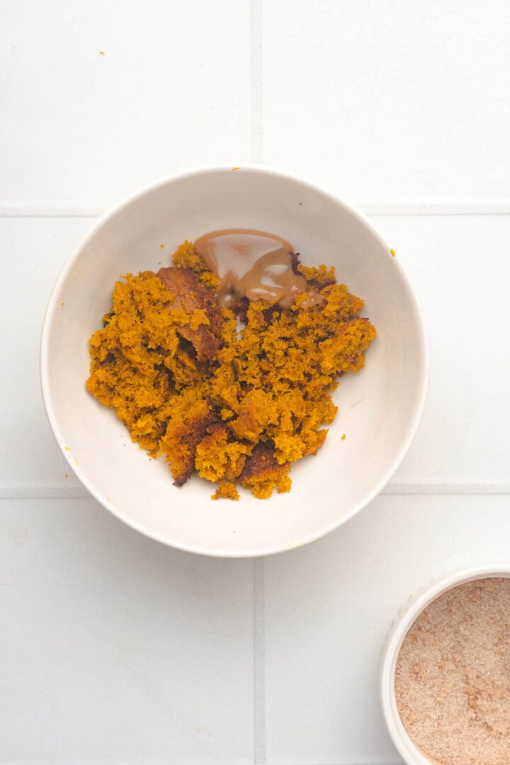 A white bowl with mashed sweet potato and a dollop of brown paste sits on a white tiled surface, reminiscent of the warm, comforting flavors found in Salted Caramel Pumpkin Muffins.