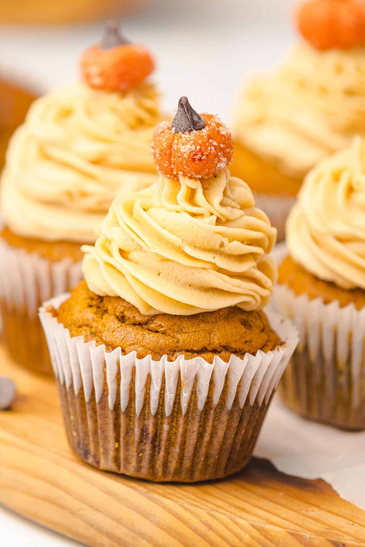 Pumpkin cupcakes with swirled frosting, topped with a small candy pumpkin, sit on a wooden board&mdash;perfect for fall or as a sweet twist on Salted Caramel Pumpkin Muffins.