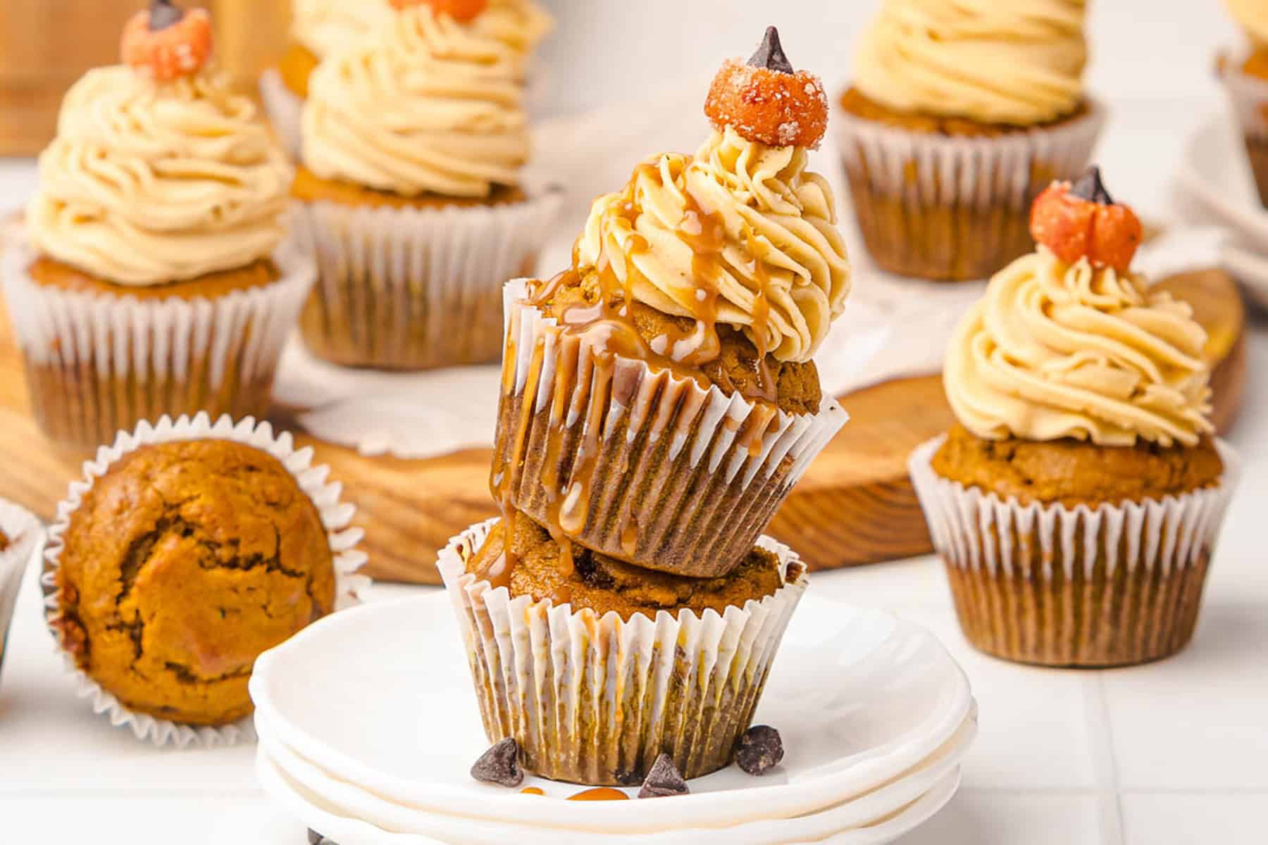 Two pumpkin cupcakes stacked, topped with swirled frosting, caramel drizzle, and mini pumpkin candies&mdash;these treats are reminiscent of decadent Salted Caramel Pumpkin Muffins.