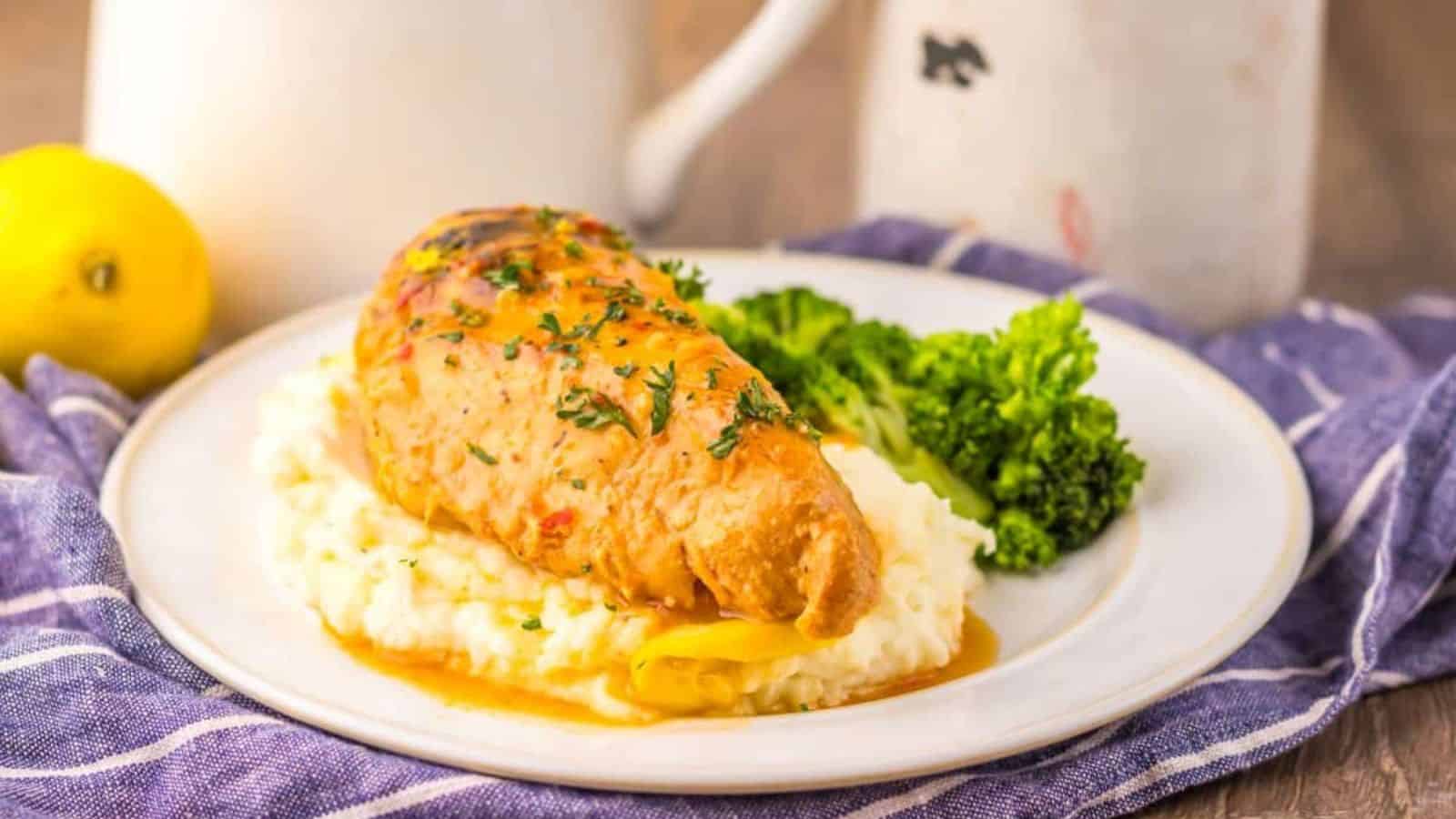 A stuffed chicken breast topped with herbs is served on mashed potatoes with a side of steamed broccoli on a white plate.