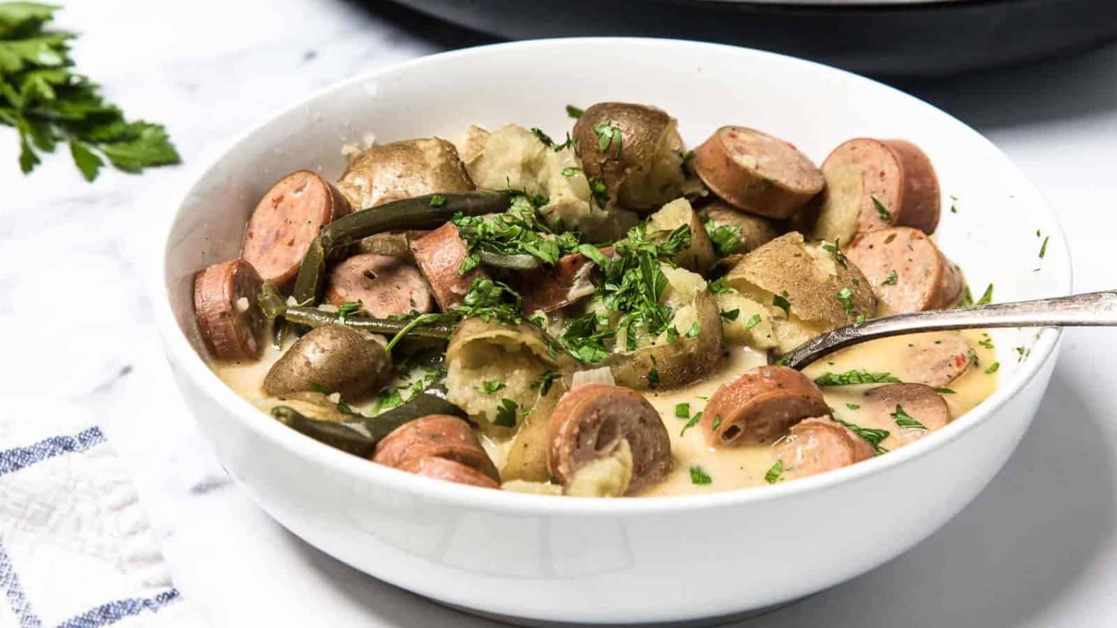 A bowl of sausage, potatoes, and green beans garnished with chopped parsley.