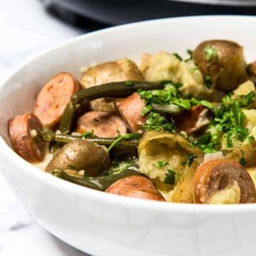 A bowl of sausage, potatoes, and green beans garnished with chopped parsley.