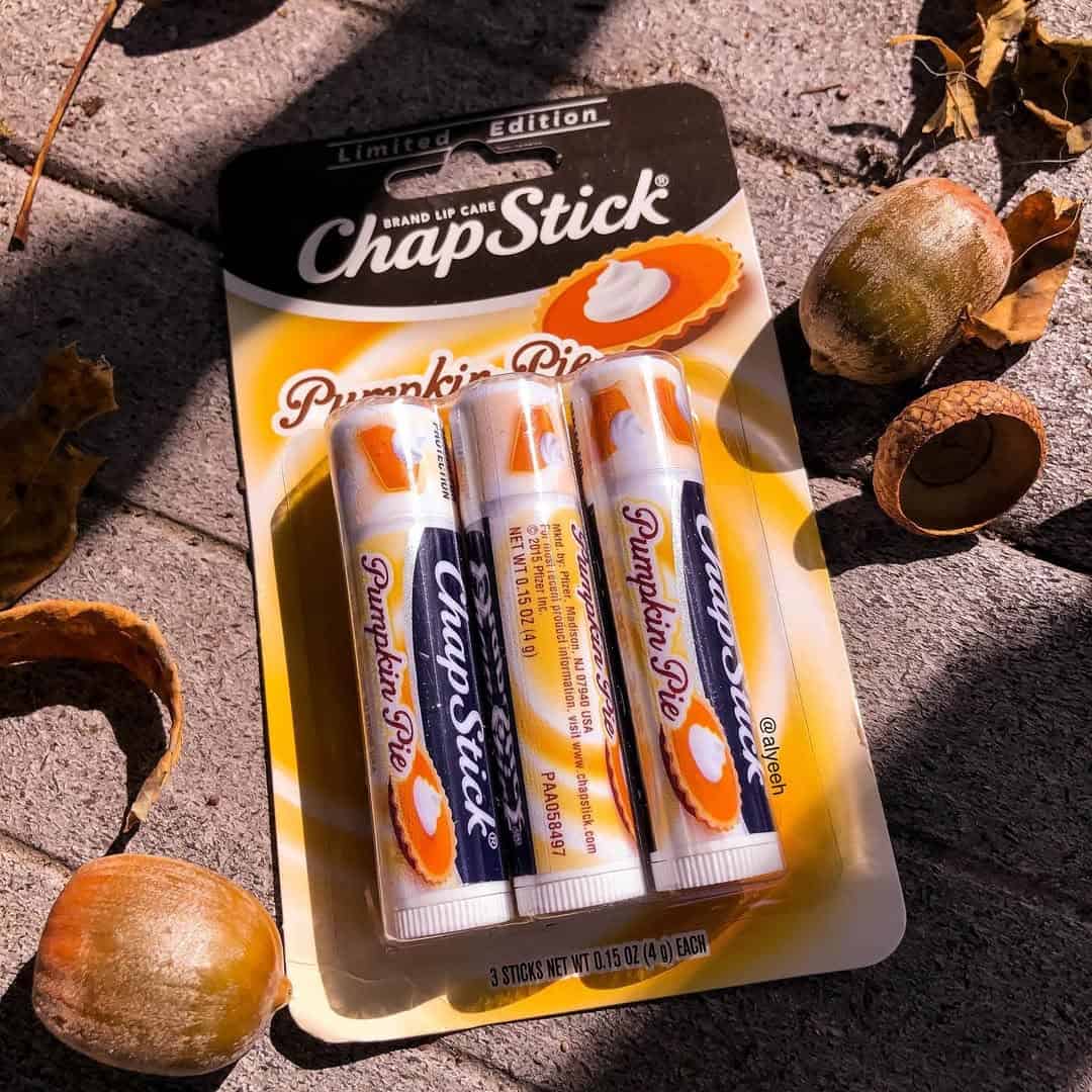 Three tubes of limited edition Pumpkin Pie ChapStick on a sidewalk with acorns and leaves around them.