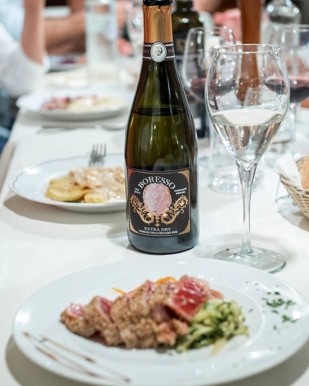 A bottle of sparkling wine on a table set with plates of food, a wine glass, and cutlery—perfect gifts for holiday hosts and entertainers.