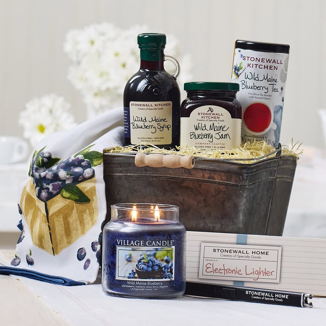 A cozy holiday gift basket featuring blueberry-themed syrup, jam, tea, a candle, towel, and an electronic lighter—perfect for warming up any winter day.