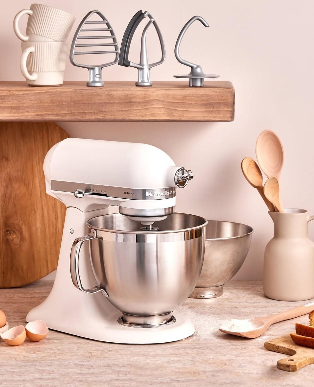 A white stand mixer with a metal bowl on a kitchen counter, surrounded by baking tools and ingredients.