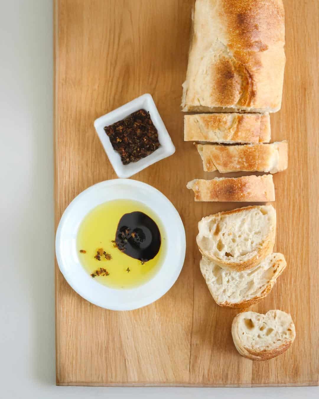 Sliced bread with olive oil, balsamic vinegar, and spices on a wooden board-perfect for Gifts for Holiday Hosts and Entertainers.