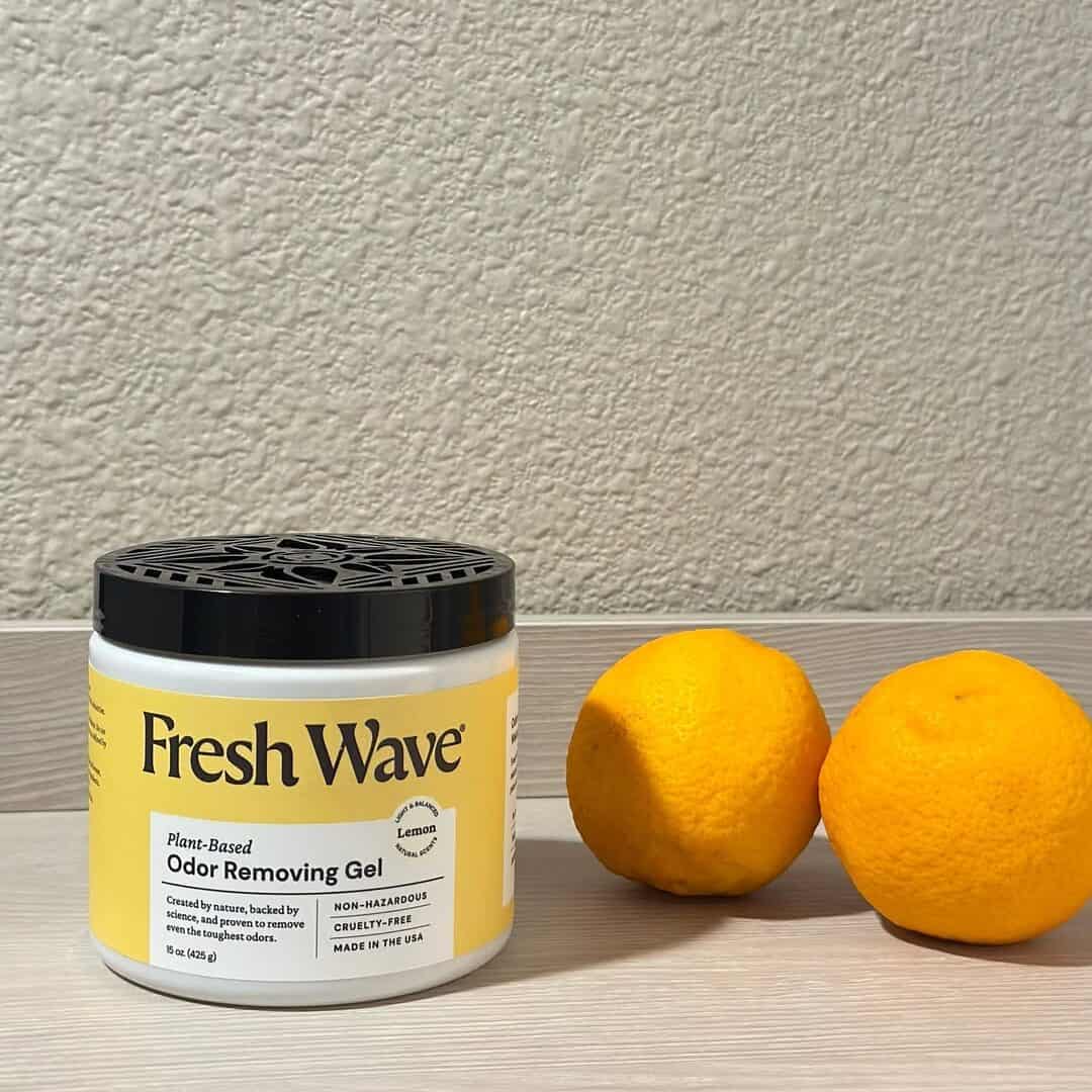 A Fresh Wave odor removing gel container next to two lemons on a wooden surface against a textured wall—one of those Gifts That Make Holiday Cleanup Easier.