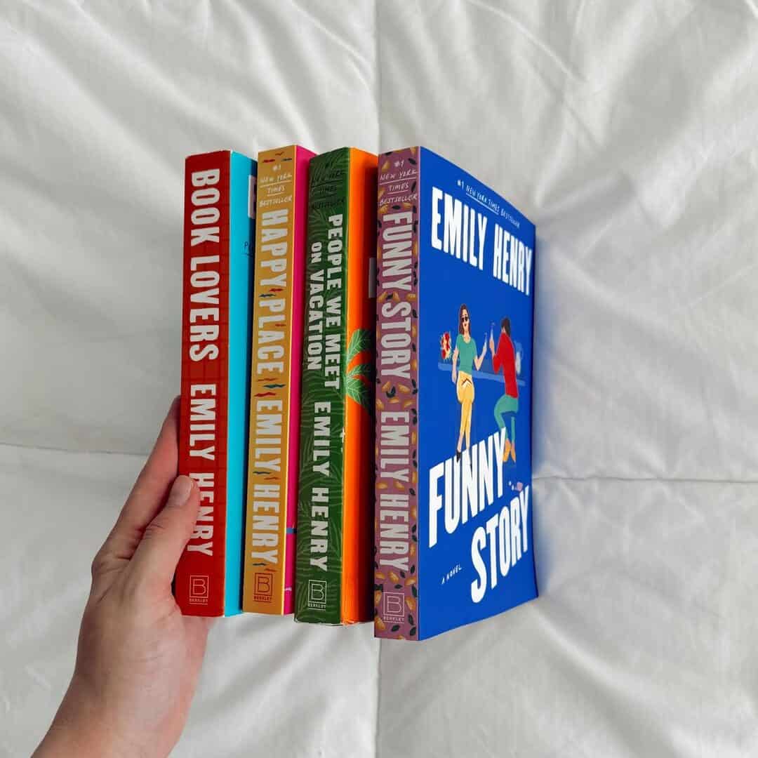 A hand holds four Emily Henry books—Book Lovers, Happy Place, People We Meet on Vacation, and Funny Story—perfect cozy holiday gifts for any book lover.