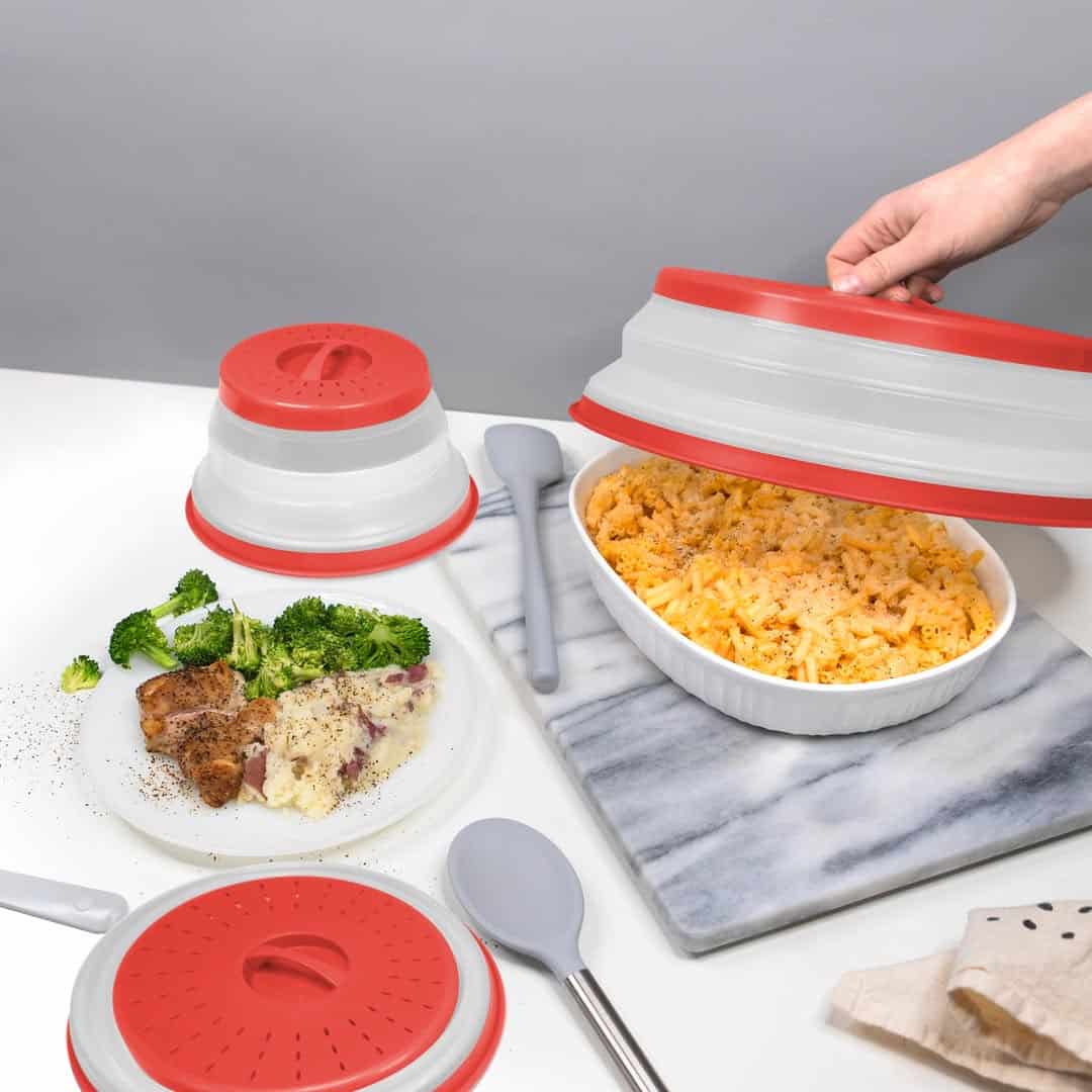 A hand lifts a red-lidded cover from a dish of macaroni near a plate of food and kitchen utensils—one of those Gifts That Make Holiday Cleanup Easier.