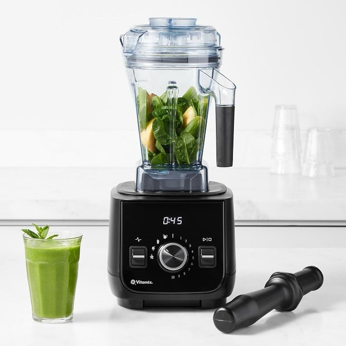 A black blender with spinach and apples inside sits on the counter, next to a glass of green smoothie and a tamper—perfect for those seeking Gifts That Make Holiday Cleanup Easier.