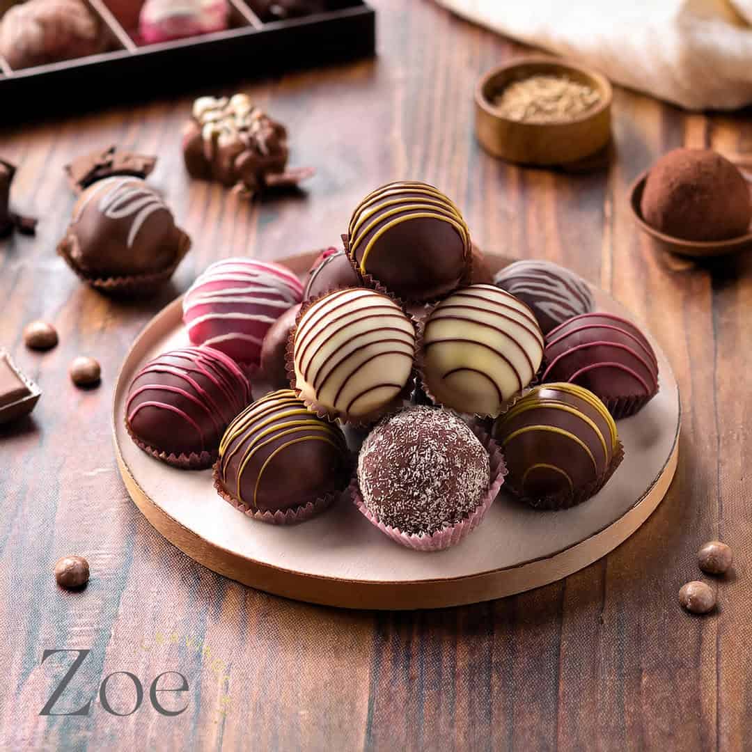 A plate of assorted gourmet chocolate truffles with decorative drizzles sits on a wooden table—perfect gifts for holiday hosts and entertainers.