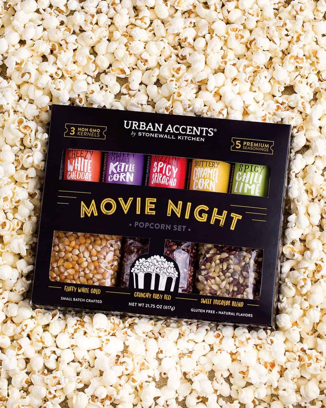 A popcorn set with assorted kernels and seasonings, placed on a bed of popped popcorn—perfect for cozy holiday gifts.