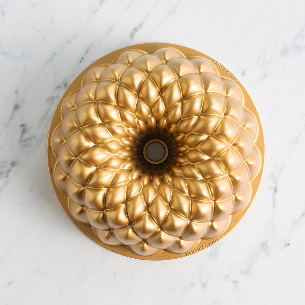 A Bundt cake with a golden, intricate, flower-like pattern-made using the best kitchen tools for holiday baking-sits on a white marble surface.