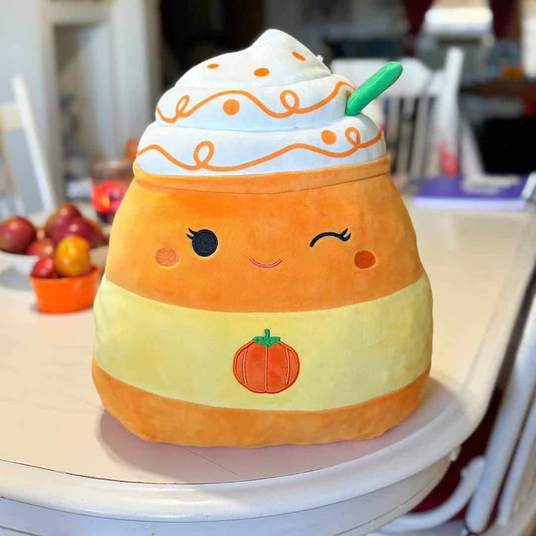 Plush pumpkin spice latte toy with whipped cream, winking face, and pumpkin embroidery on a table—perfect for fall decor or as a cute addition to your pumpkin spice gifts collection.