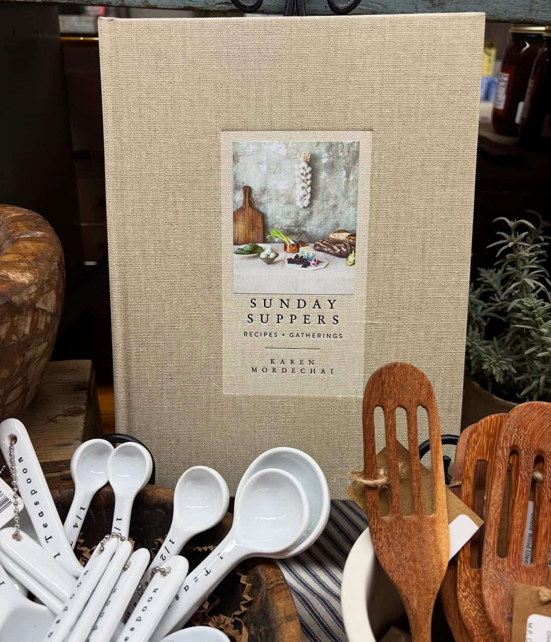 A beige cookbook titled "Sunday Suppers" stands behind measuring spoons and wooden utensils—an ideal pick among gifts for holiday hosts and entertainers.