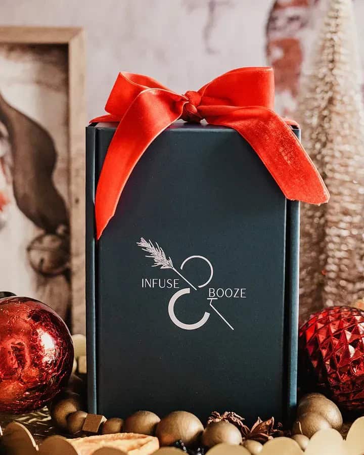 A gift box with a red bow labeled "Infuse & Booze," surrounded by ornaments and festive decor-perfect for gifts for holiday hosts and entertainers.