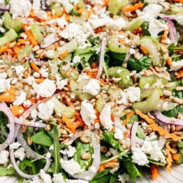 A salad with leafy greens, feta cheese, shredded carrots, onions, sunflower seeds, and dressing on a plate.