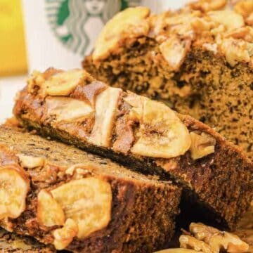 Sliced banana bread topped with banana chips and walnuts, with a Starbucks cup in the background.