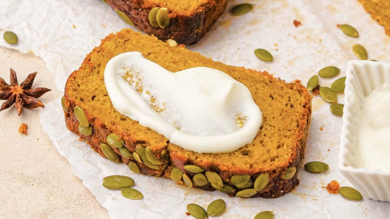 A hand picking up a slice of pumpkin bread topped with pumpkin seeds from a stacked loaf.