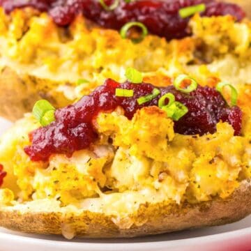 Twice-baked potatoes topped with stuffing, cranberry sauce, and chopped green onions on a white plate.