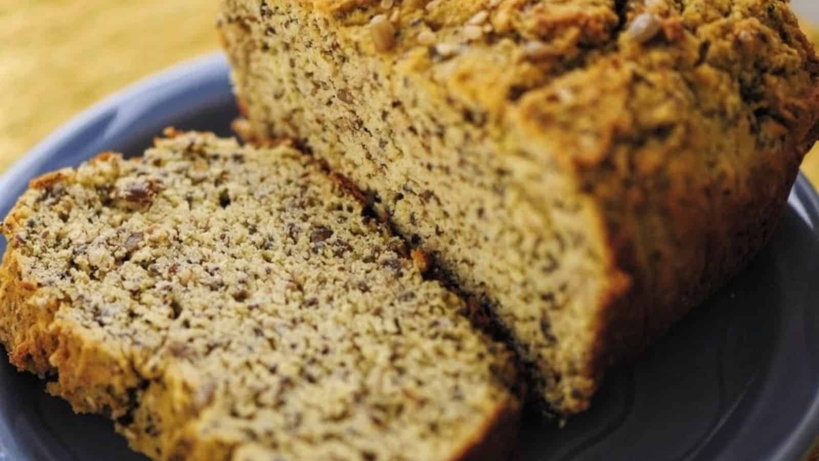 A loaf of banana nut bread with one slice cut and placed on a blue plate.