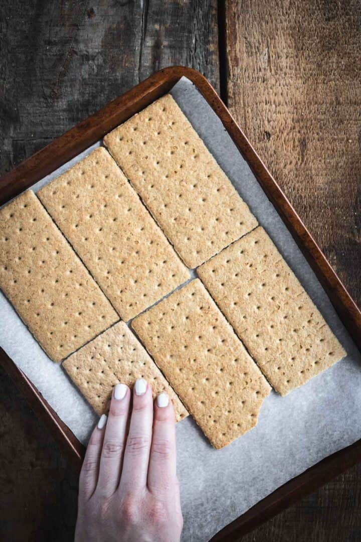 A hand grabbing a piece of Christmas Toffee Bark from a tray lined with parchment paper on a wooden surface.