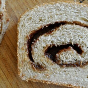A slice of cinnamon swirl bread on a wooden cutting board next to a cooling rack.