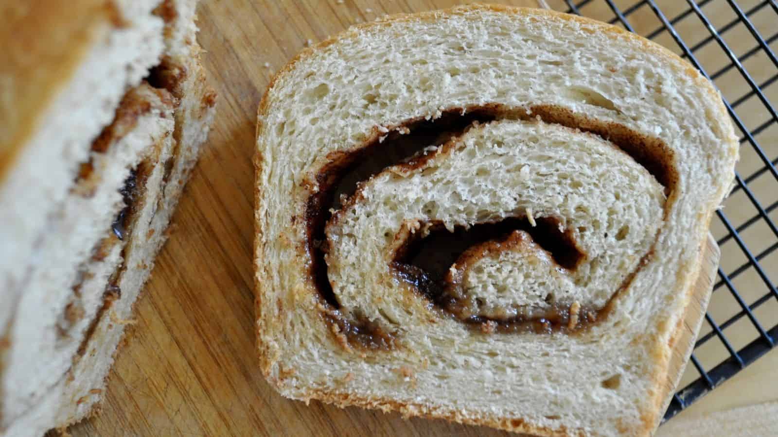 A slice of cinnamon swirl bread on a wooden cutting board next to a cooling rack.