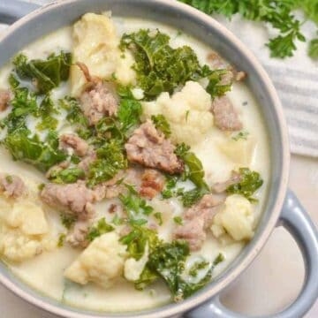 Creamy soup with sausage, kale, and cauliflower served in a bowl, topped with fresh parsley.