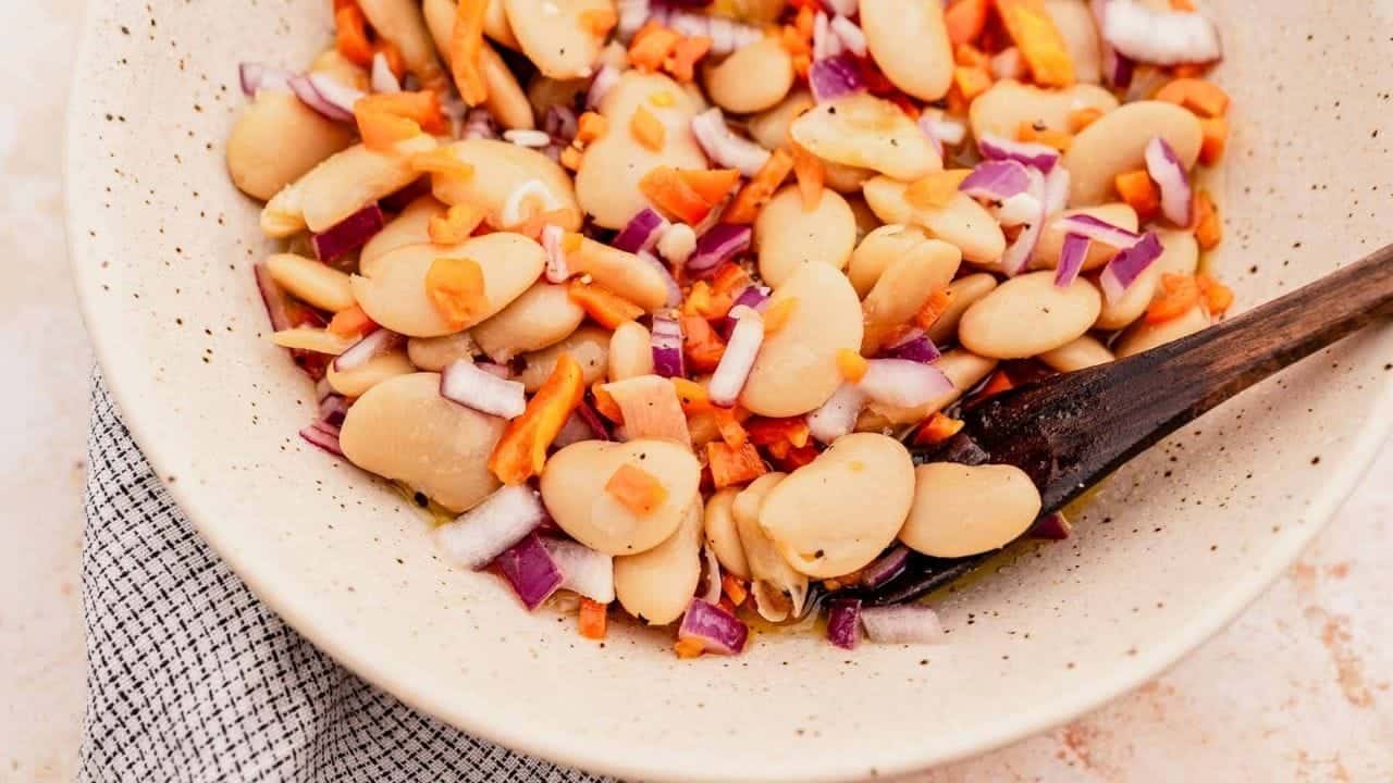 A bowl of lima bean salad with chopped carrots, red onion, and a wooden spoon.