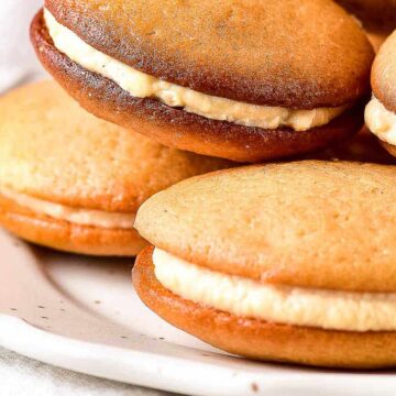 Golden whoopie pies with cream filling stacked on a white plate.