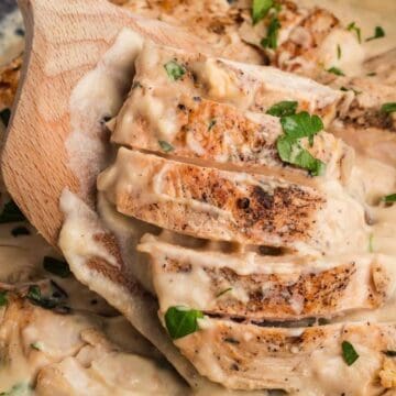 Sliced chicken breast in a creamy sauce, garnished with chopped parsley, on a wooden spatula.