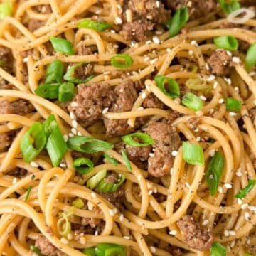 Close-up of spaghetti with ground beef, sliced green onions, sesame seeds, and black pepper on a white plate.