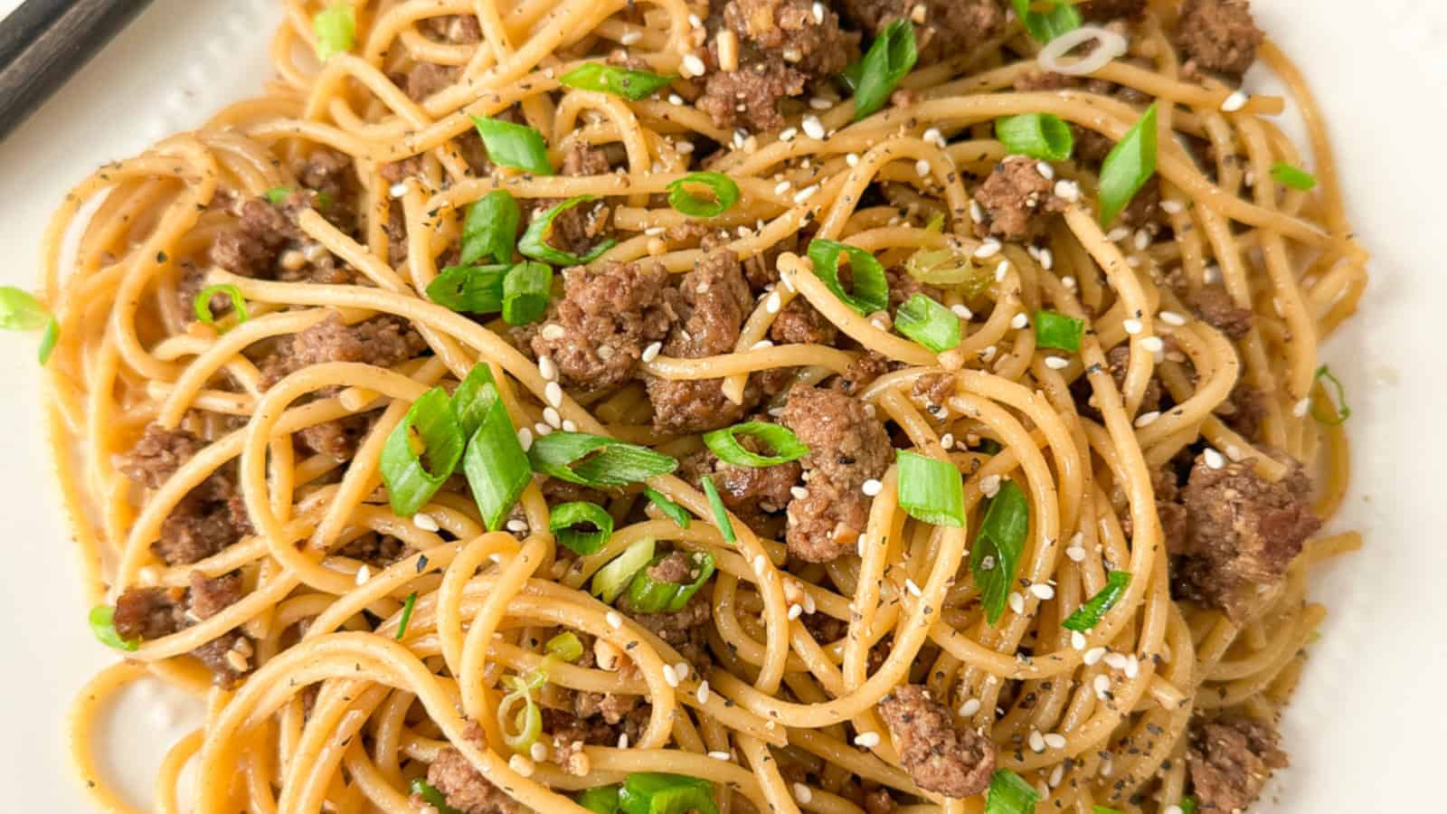 A plate of Chinese Mongolian beef noodles garnished with fresh green onions and roasted sesame seeds.