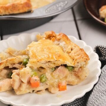 A slice of chicken pot pie with vegetables on a white plate, next to a black and white napkin.