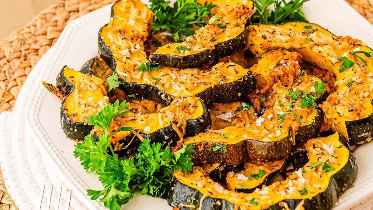 Roasted acorn squash slices garnished with fresh parsley and shredded cheese on a white plate.