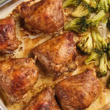 Baked chicken thighs and roasted broccoli on a sheet pan lined with parchment paper.