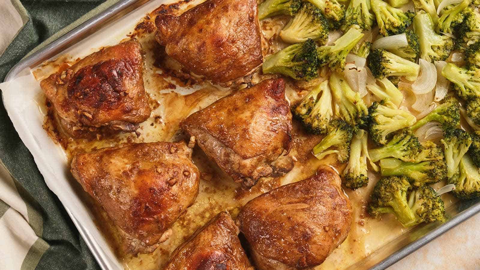 Baked chicken thighs and roasted broccoli on a sheet pan lined with parchment paper.