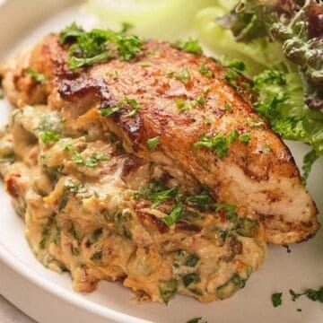 Seasoned chicken breast with creamy spinach filling, garnished with parsley, served with mixed leafy greens.