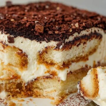 A close-up of a slice of tiramisu with layers of cream, coffee-soaked ladyfingers, and chocolate shavings.